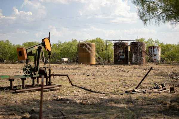 Abandoned oil well adjacent to rusting storage tanks