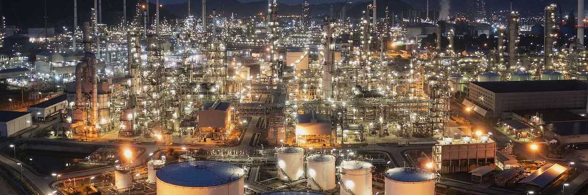 Aerial drone view of oil storage tanks in foreground with oil refinery behind.