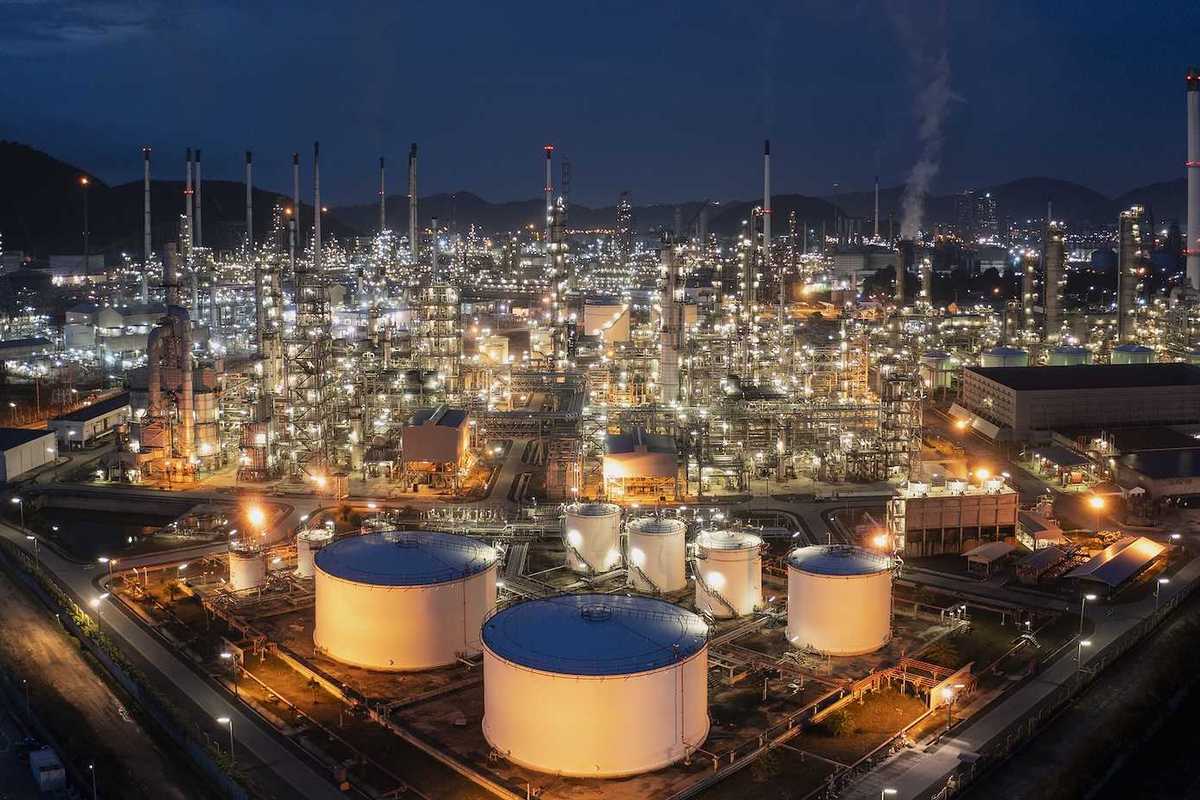 Aerial drone view of oil storage tanks in foreground with oil refinery behind.