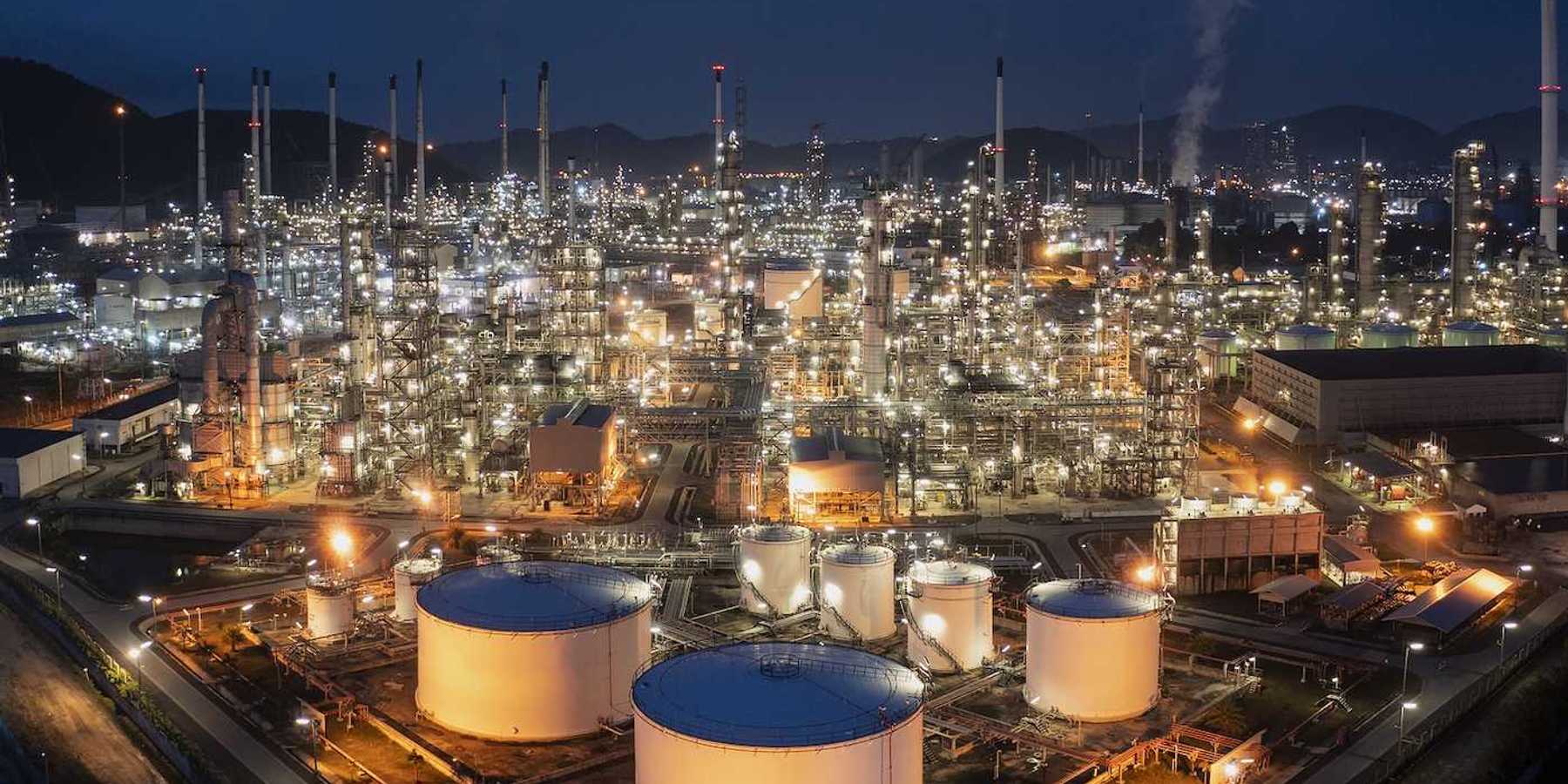 Aerial drone view of oil storage tanks in foreground with oil refinery behind.