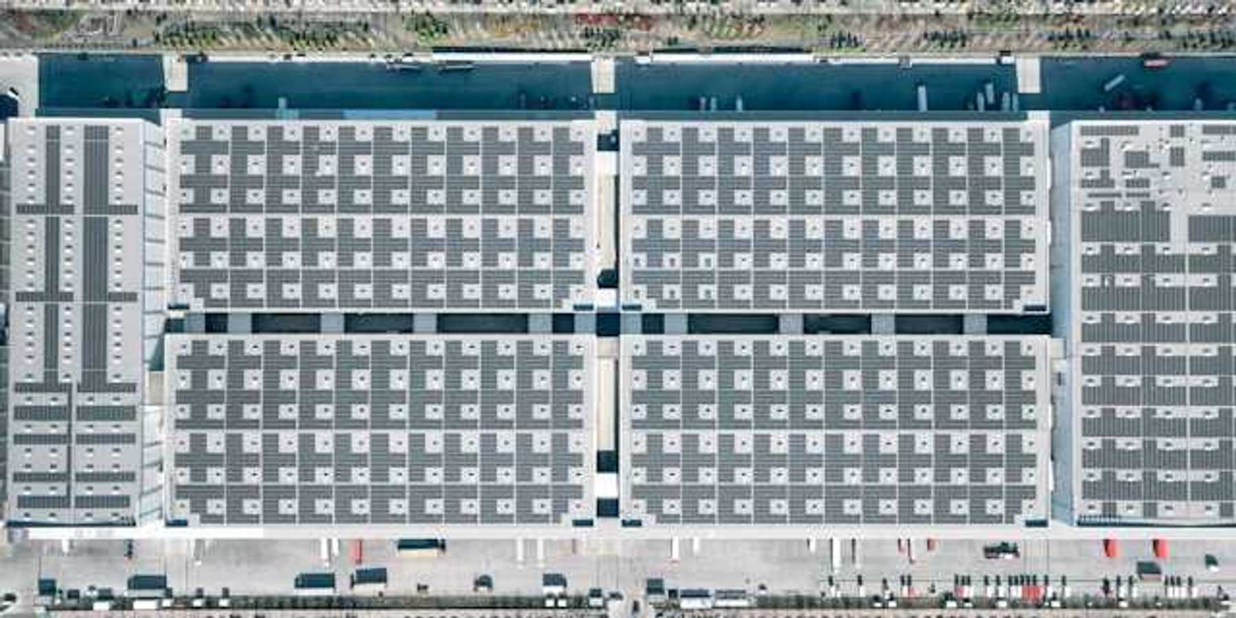 Aerial view of a city building with solar panels covering it and roads with cars on either side
