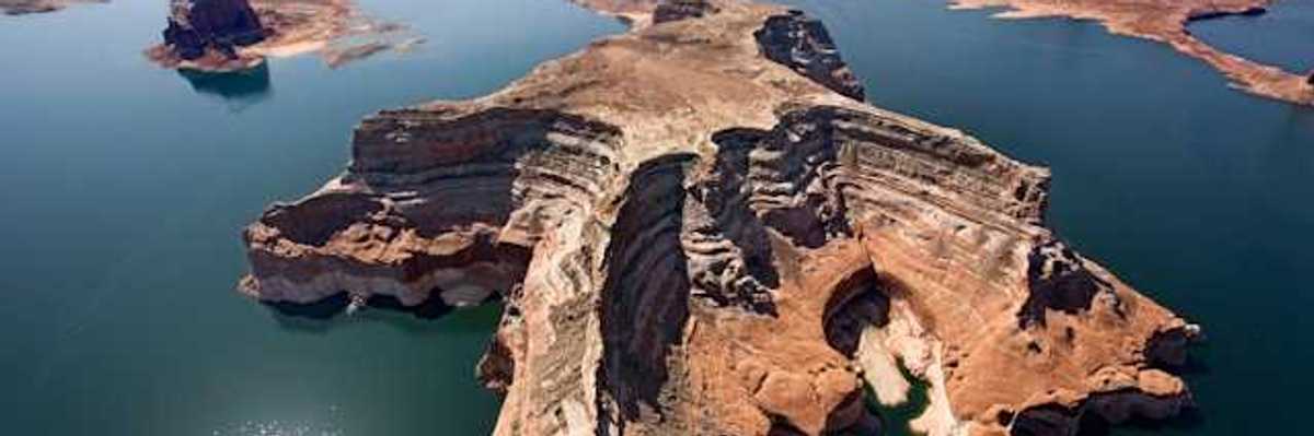Aerial view of a lake with reddish rock formations in the center and perimeter of it