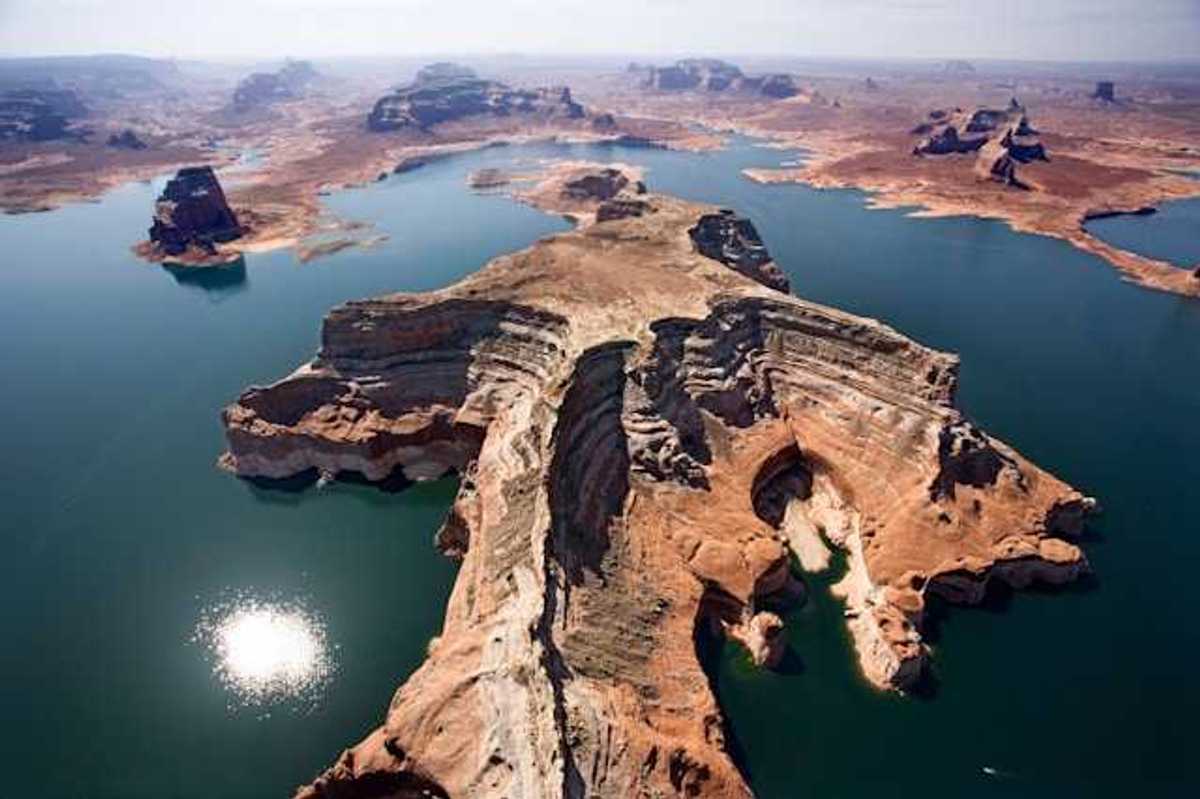 Aerial view of a lake with reddish rock formations in the center and perimeter of it