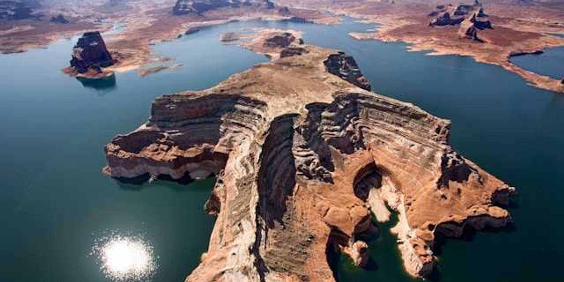 Aerial view of a lake with reddish rock formations in the center and perimeter of it