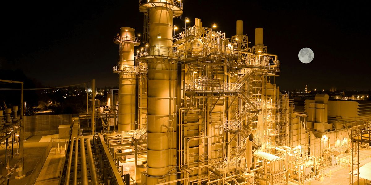 Aerial view of a refinery lit up at night with a full moon in the background.