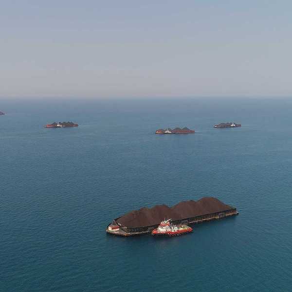 Aerial view of barges full of coal anchored at the sea near a coal-fired power station waiting be transported