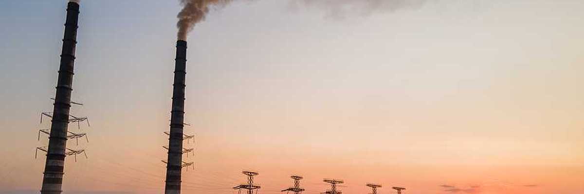 Aerial view of coal power plant with black smoke moving upwards polluting atmosphere at sunset.