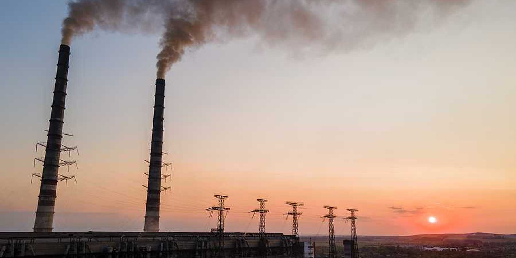 Aerial view of coal power plant with black smoke moving upwards polluting atmosphere at sunset.