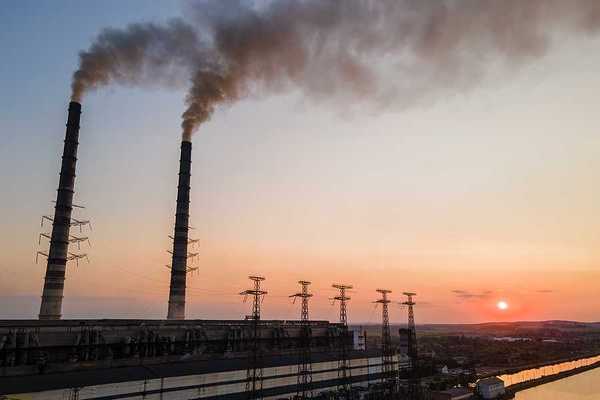 Aerial view of coal power plant with black smoke moving upwards polluting atmosphere at sunset.