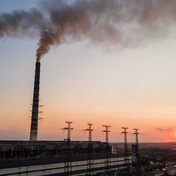 Aerial view of coal power plant with black smoke moving upwards polluting atmosphere at sunset.