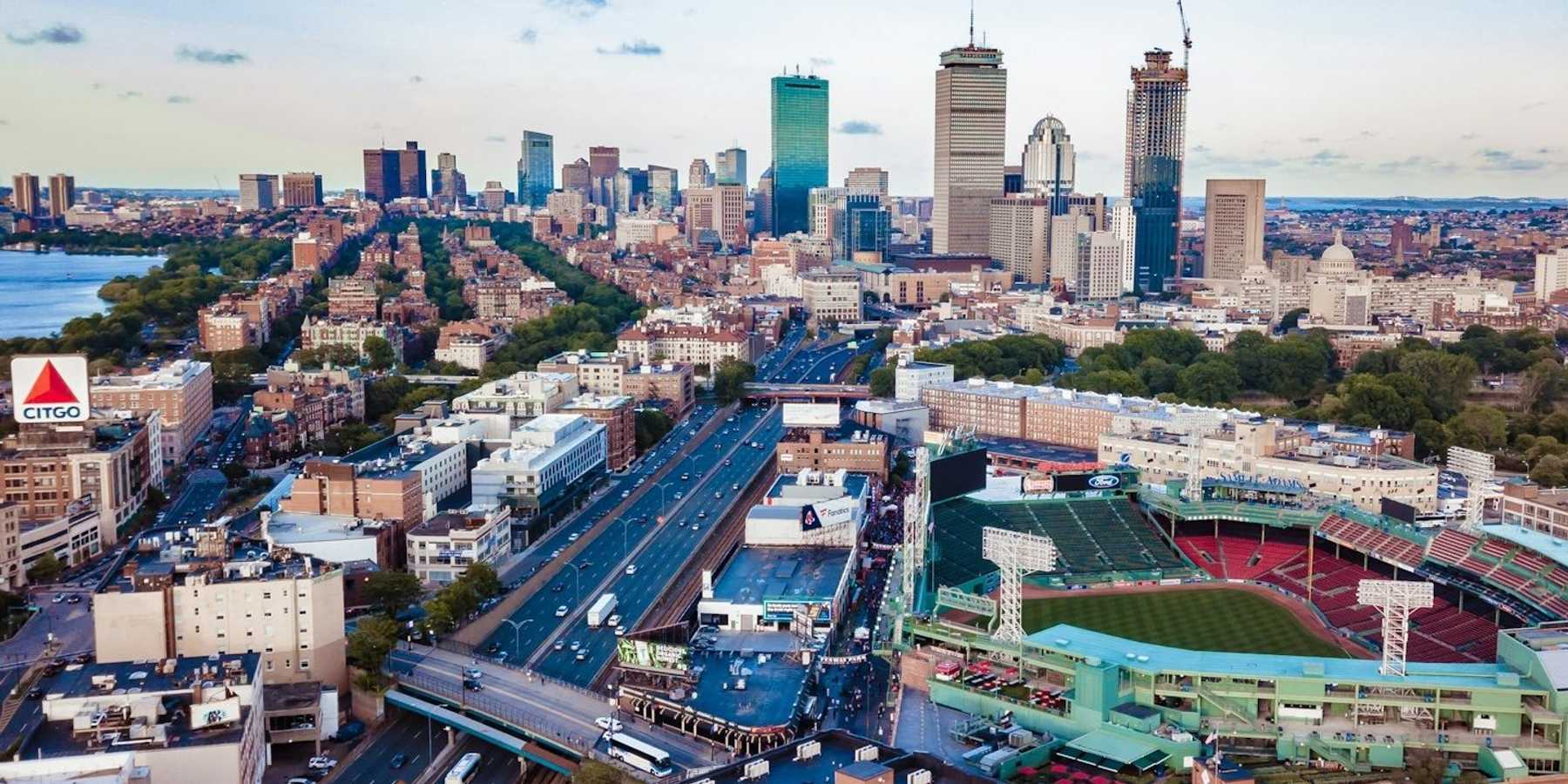 Aerial view of the Boston skyline with major highway, waterfront and stadium visible.