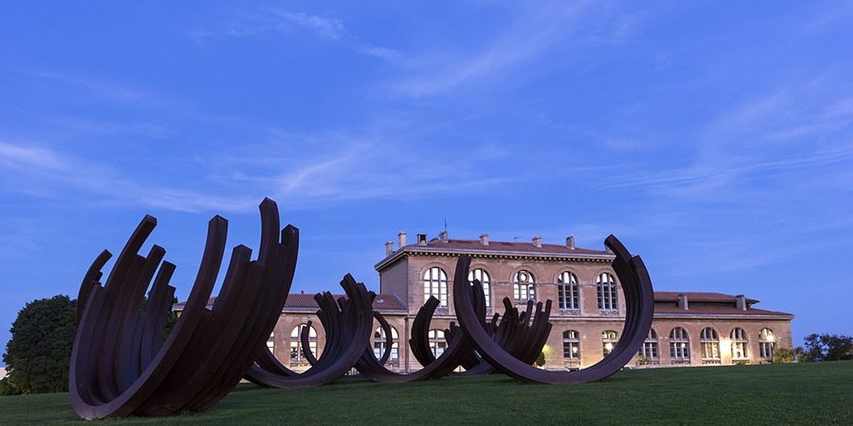 Aix-Marseille University with a green lawn and large abstract sculpture in the foreground.