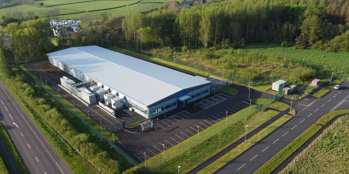 an aerial view of a data center flanked by trees, roads and green fields.