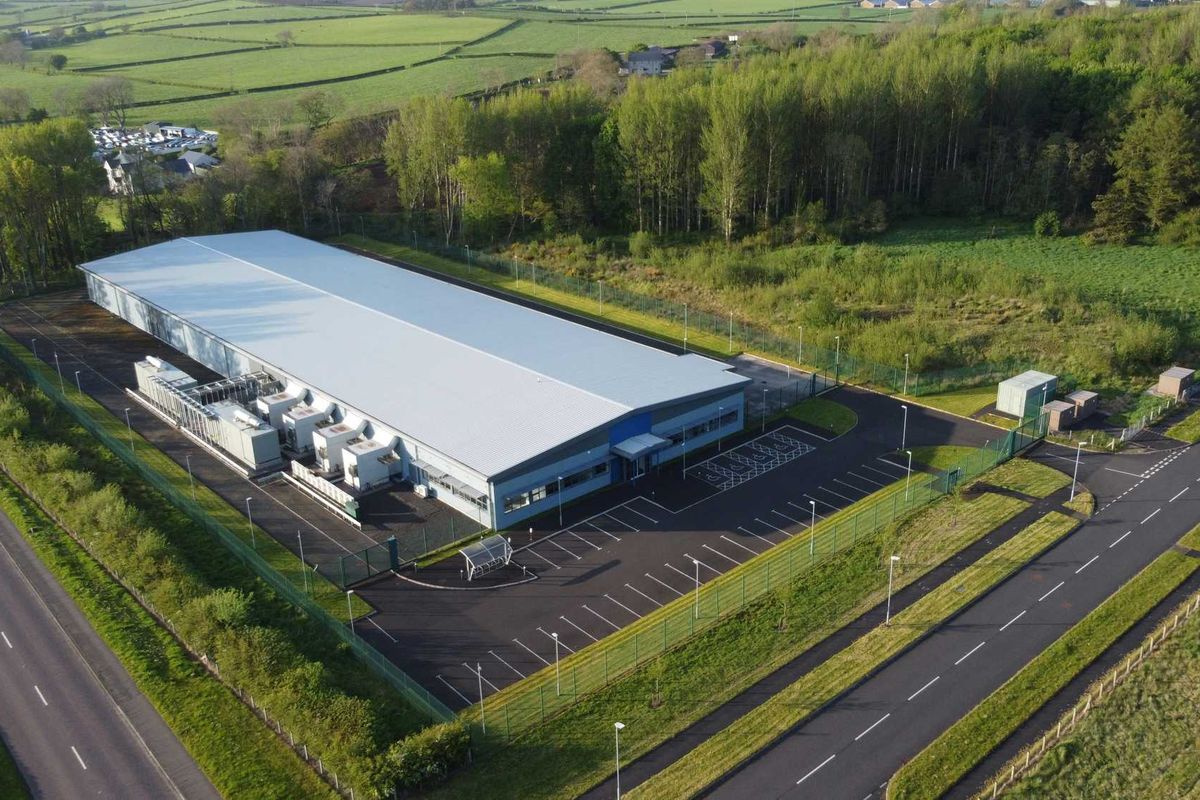 an aerial view of a data center flanked by trees, roads and green fields.
