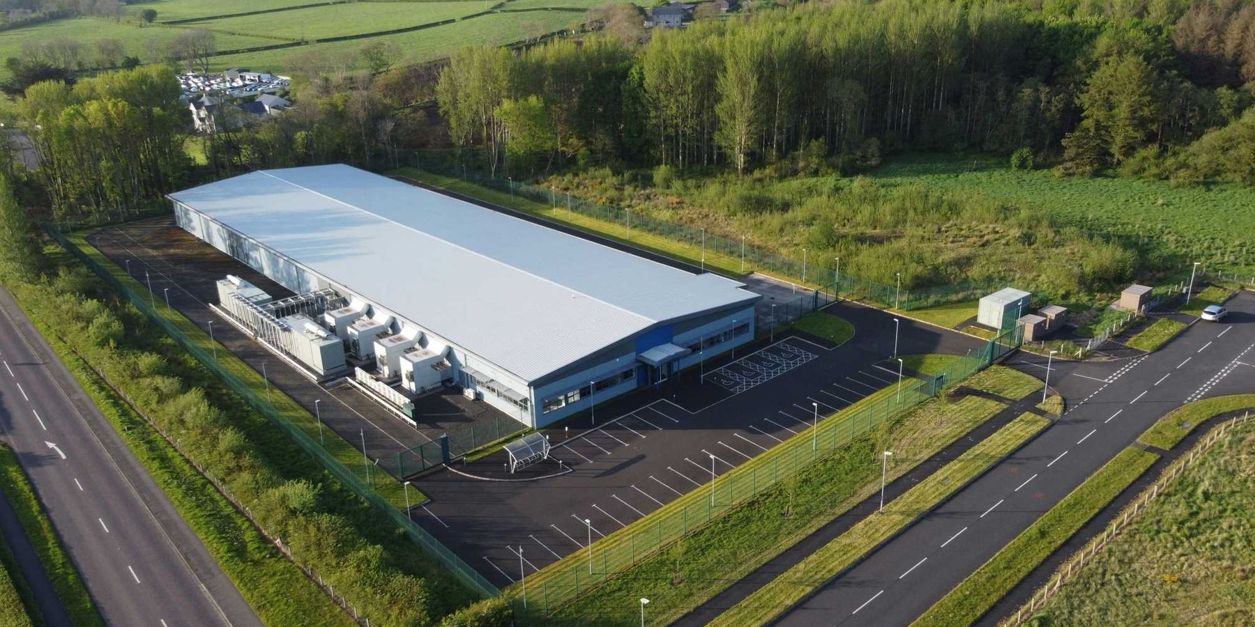 an aerial view of a data center flanked by trees, roads and green fields.