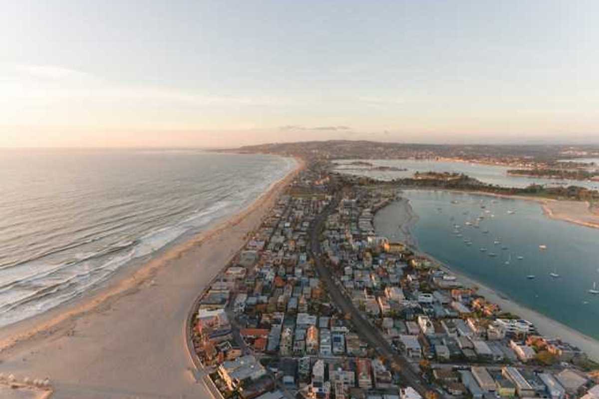 An aerial view of a peninsula with ocean on one side and a harbor on the other with houses on the land