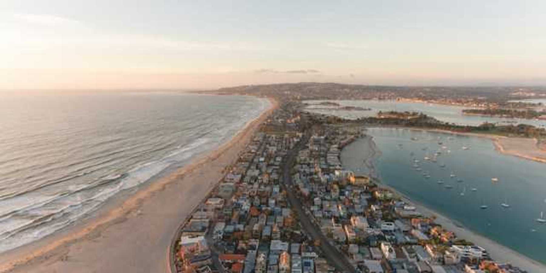 An aerial view of a peninsula with ocean on one side and a harbor on the other with houses on the land