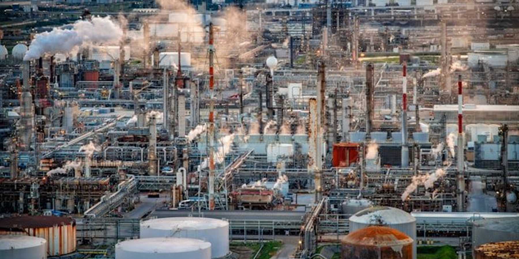 An aerial view of a refinery with a city in the background.