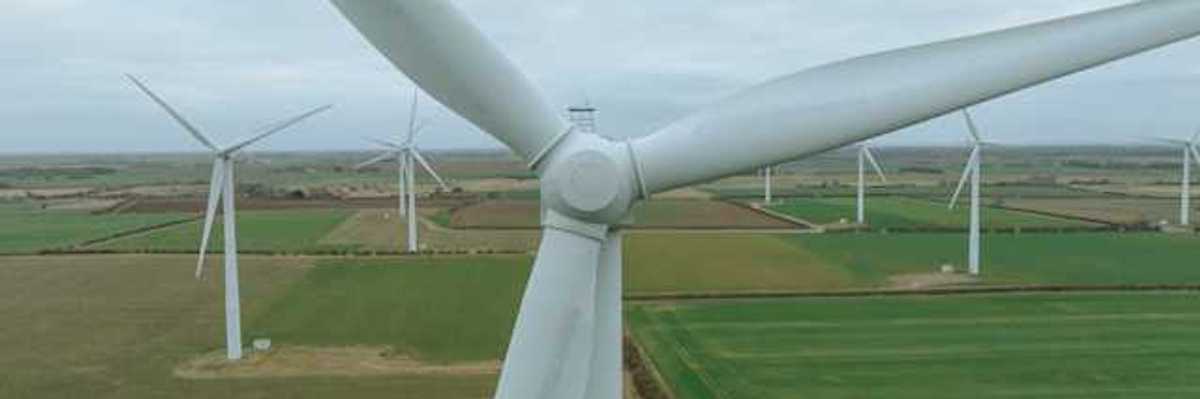 An aerial view of a row of wind turbines situated in a green field