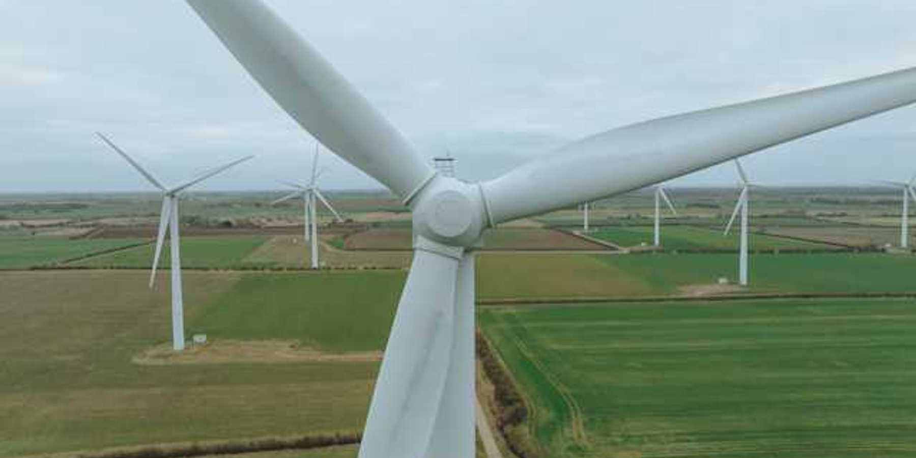 An aerial view of a row of wind turbines situated in a green field