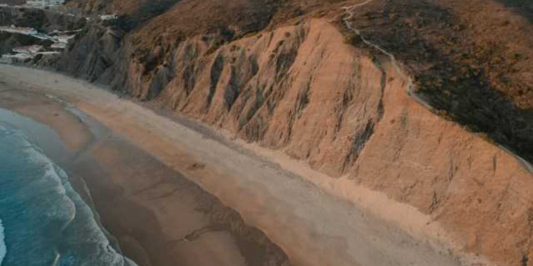 An aerial view of a sandy beach and a cliff