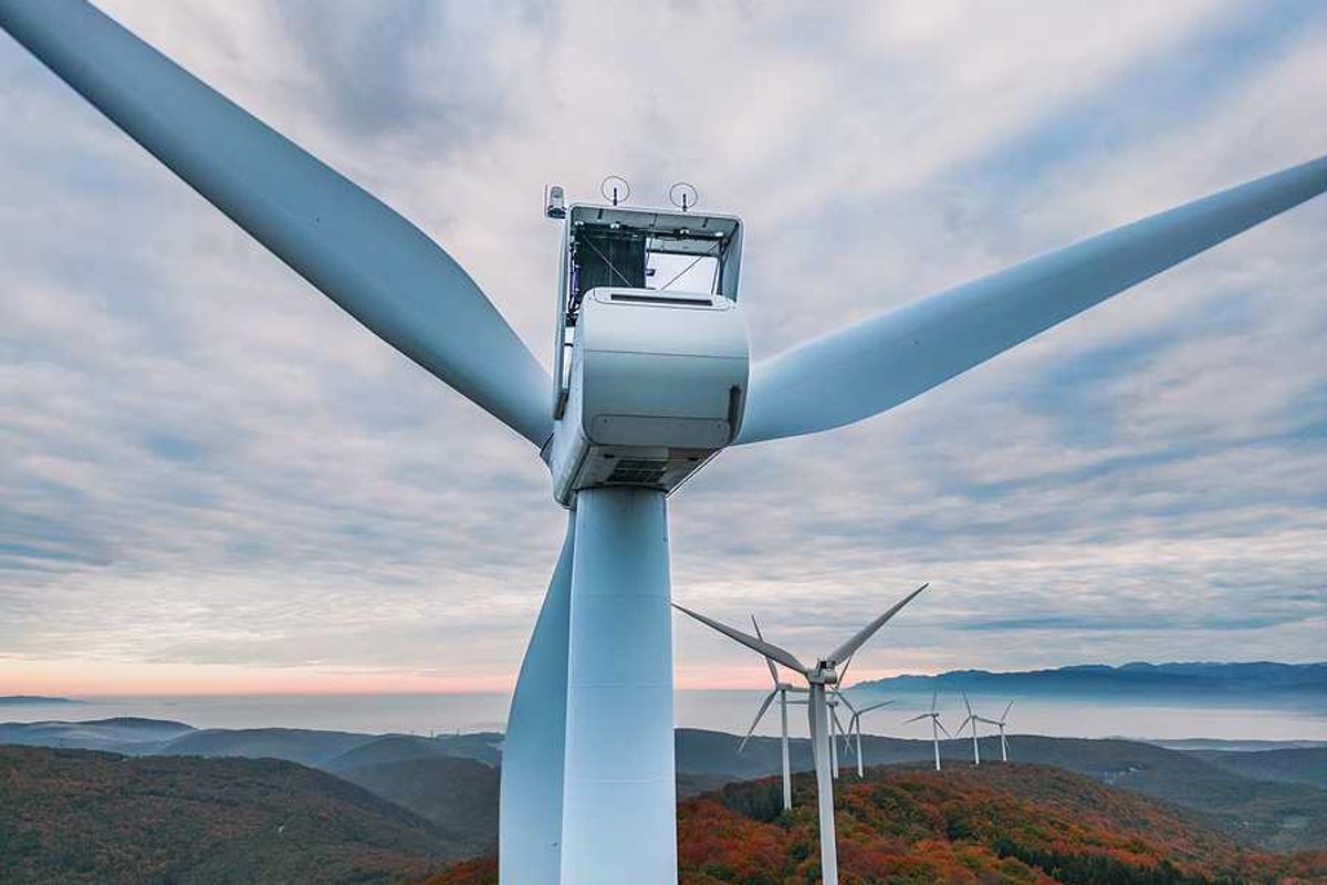 An aerial view of a set of wind turbines atop forested hills