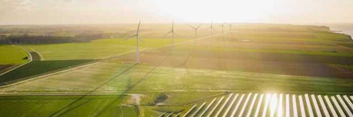 An aerial view of a solar farm with wind turbines in the background