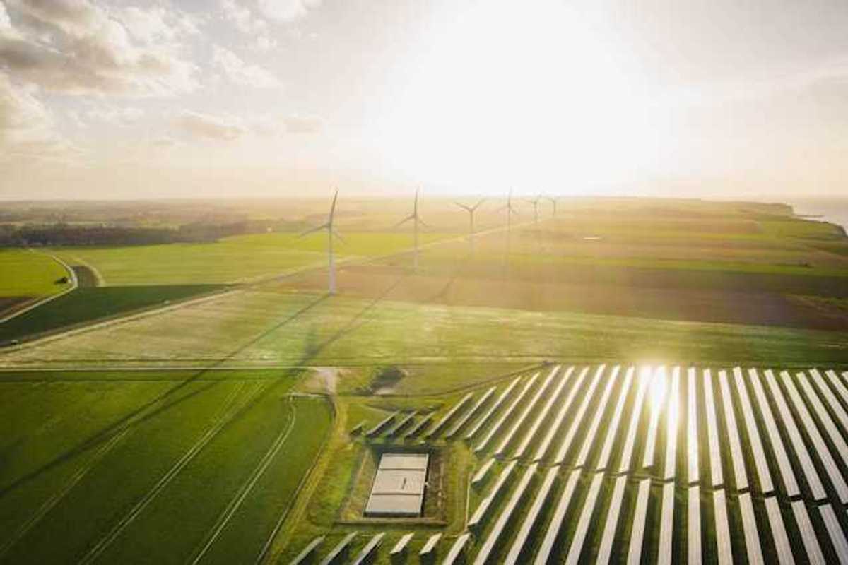An aerial view of a solar farm with wind turbines in the background