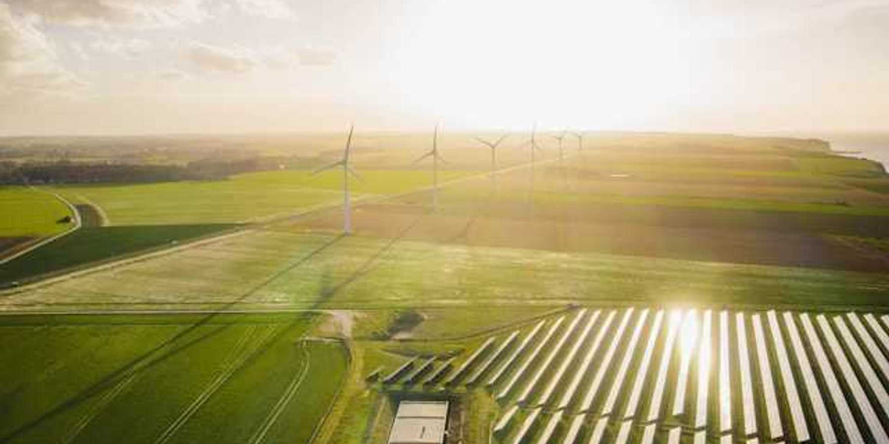 An aerial view of a solar farm with wind turbines in the background