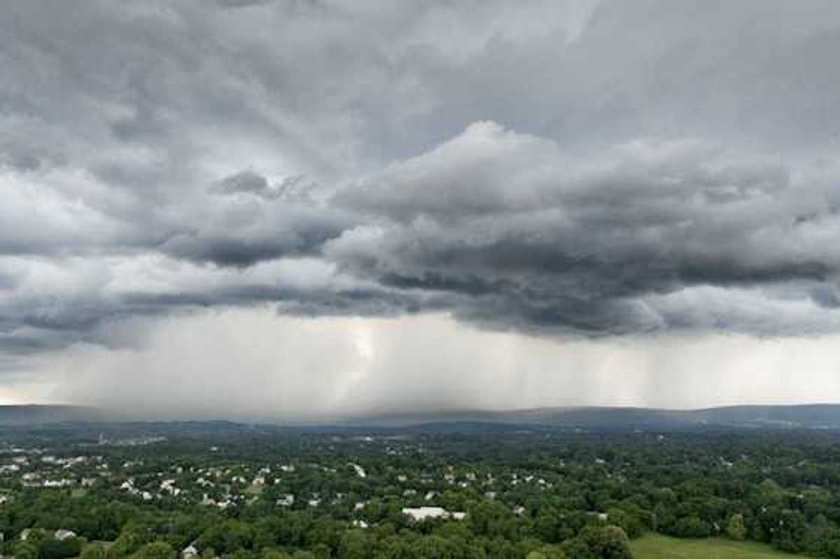 An aerial view of a town surrounded by green trees with a huge storm in the distance