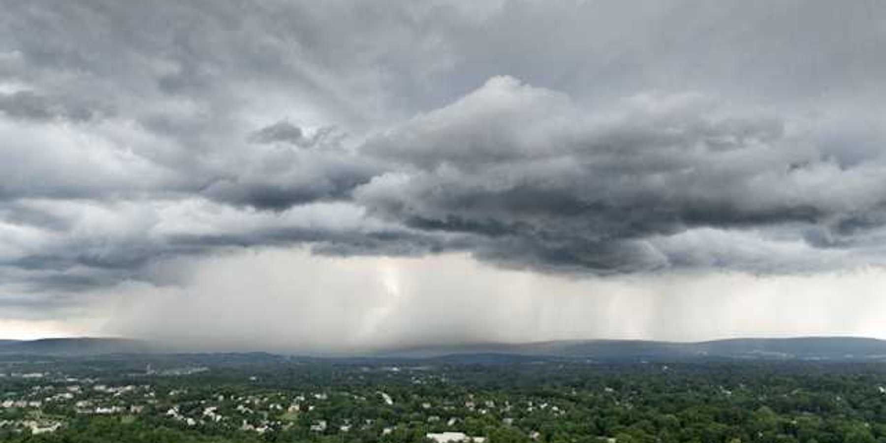 An aerial view of a town surrounded by green trees with a huge storm in the distance
