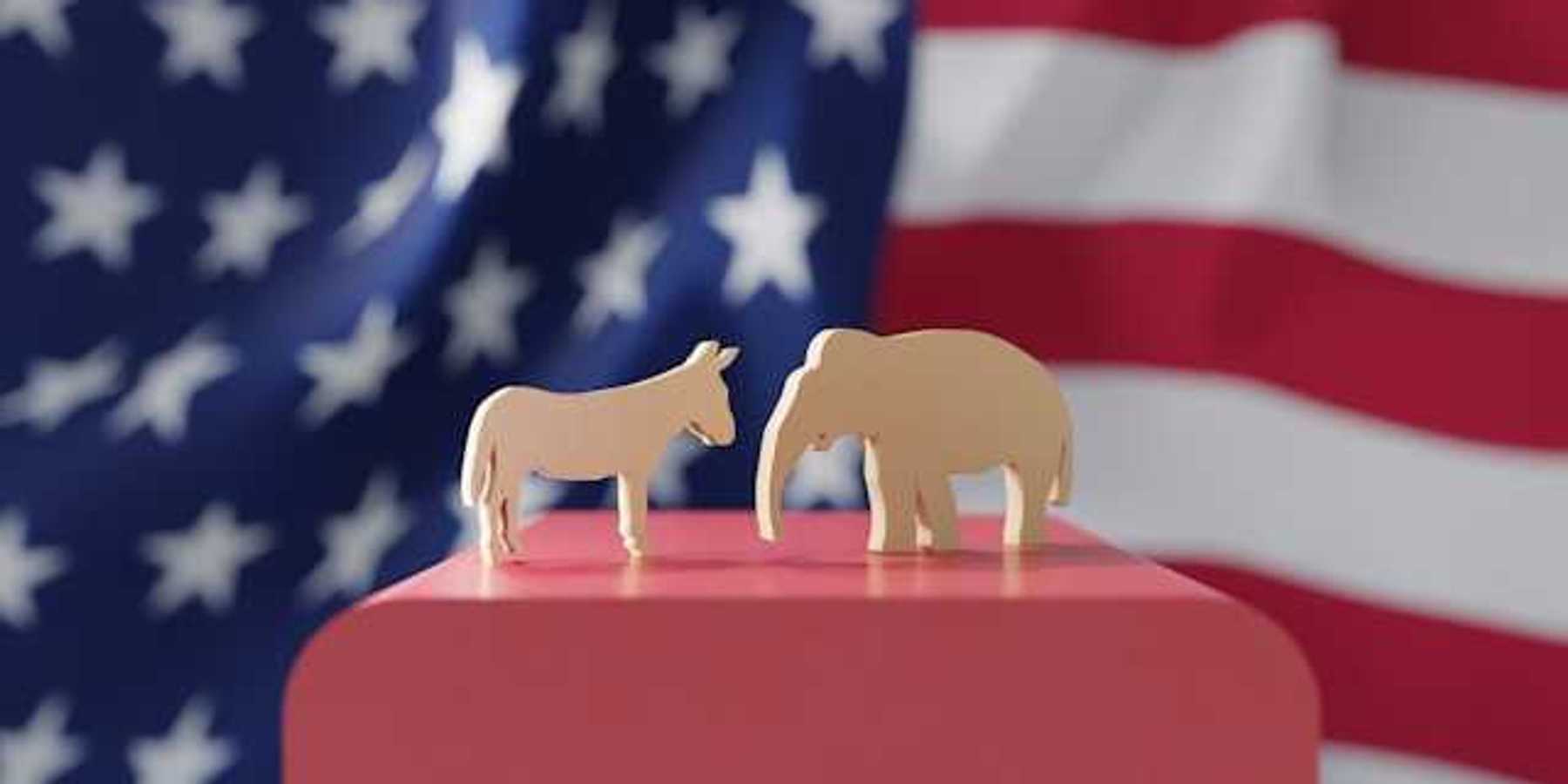 An American flag with wooden cutouts of a donkey and an elephant in the foreground