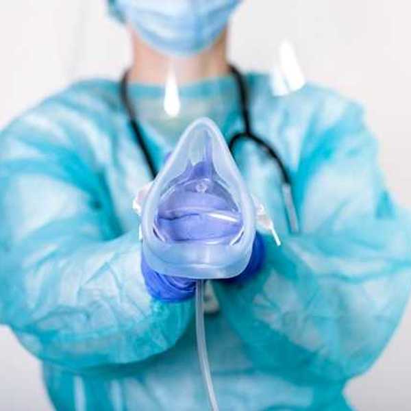 An anesthesiologist wearing a blue jumpsuit and face mask holding an anesthesia mask for a patient