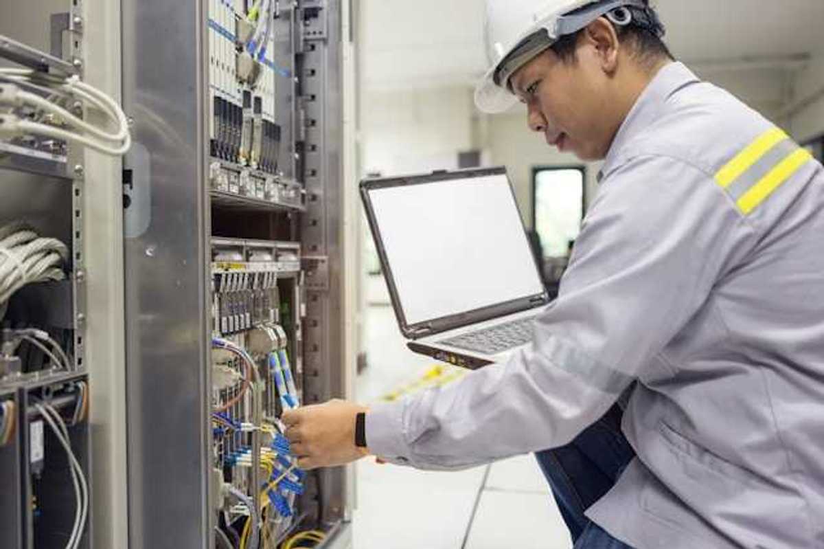 An Asian worker kneeling in front of a server with a laptop