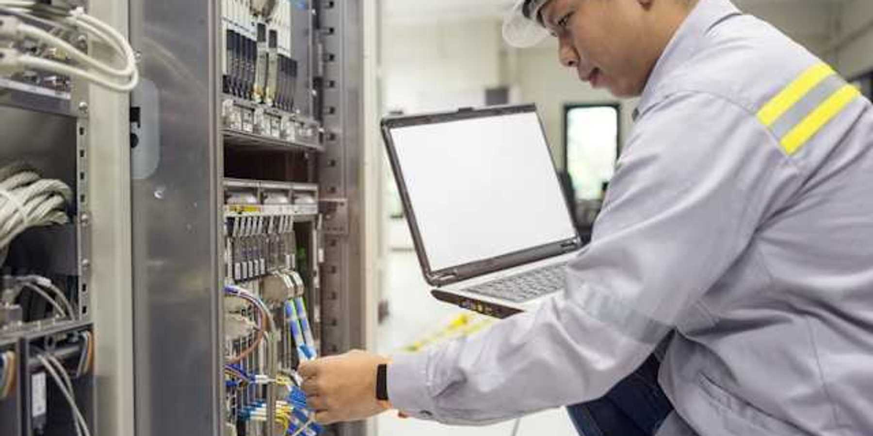 An Asian worker kneeling in front of a server with a laptop