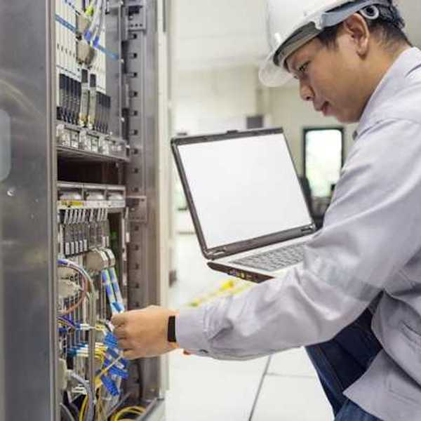 An Asian worker kneeling in front of a server with a laptop