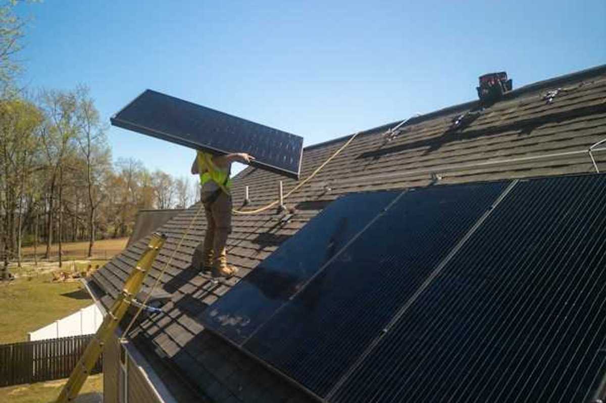 An energy worker placing solar panels on a roof