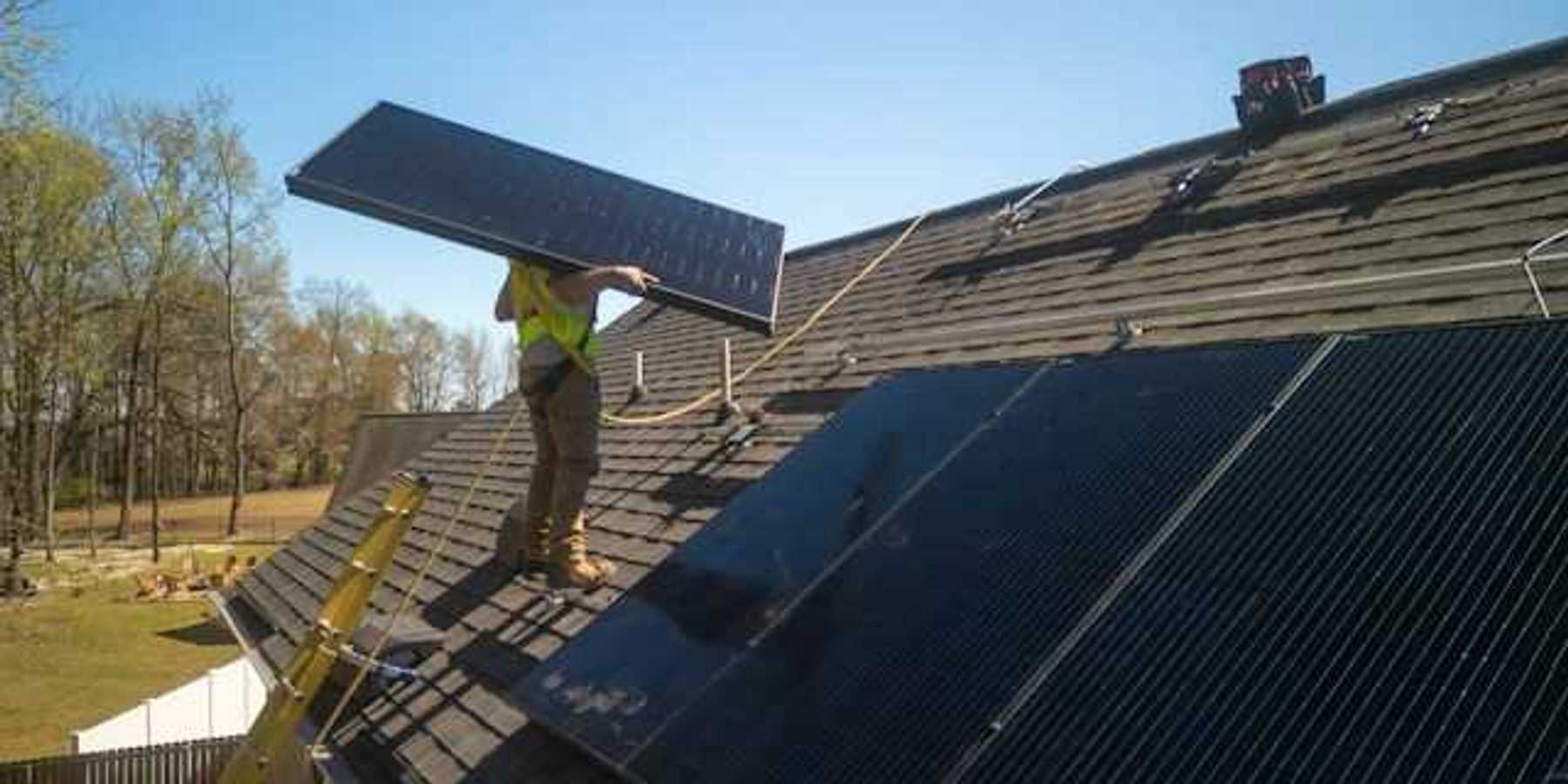 An energy worker placing solar panels on a roof