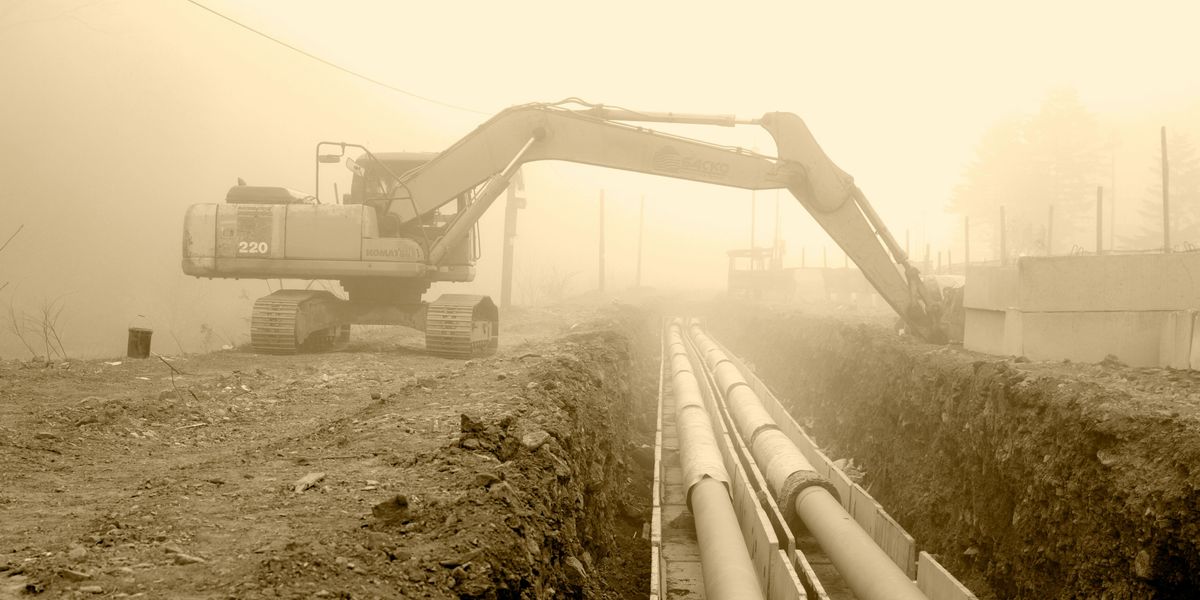 An excavator beside large pipes.