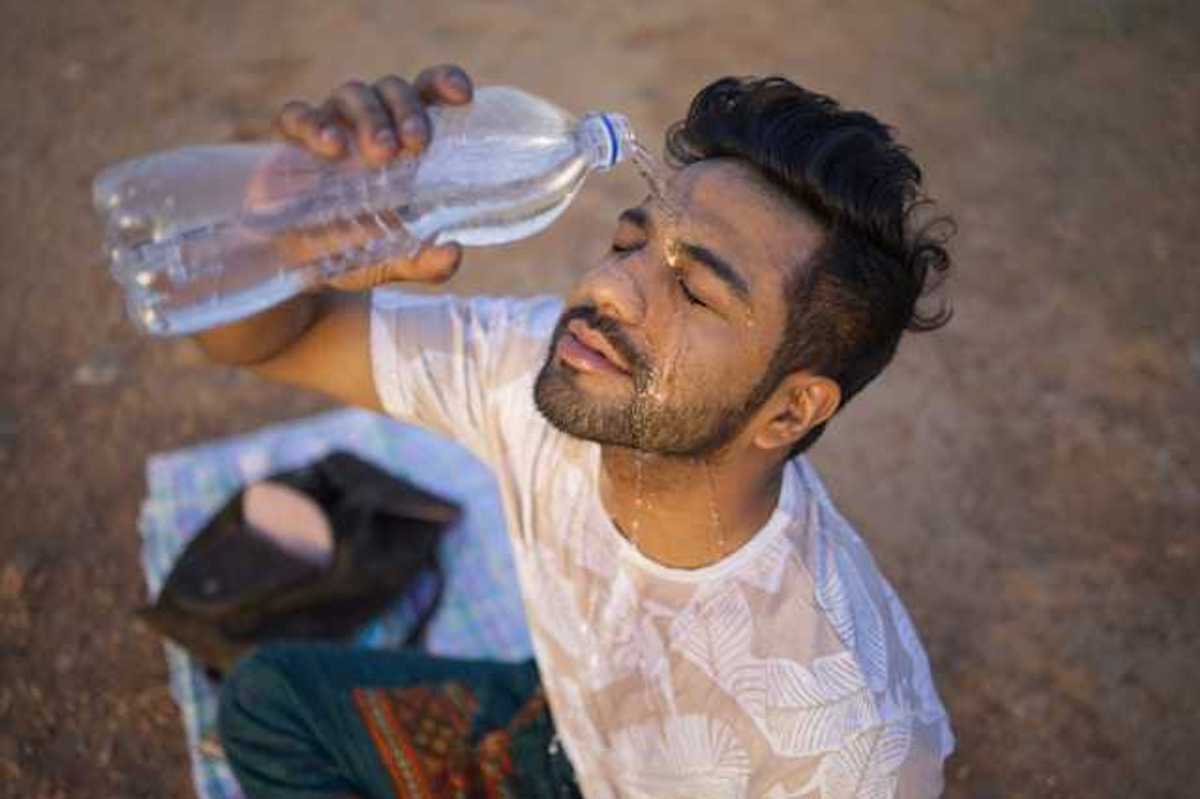 An Indian man sitting on the ground pouring a bottle of water on his face on a hot day