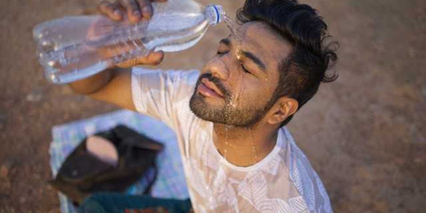 An Indian man sitting on the ground pouring a bottle of water on his face on a hot day