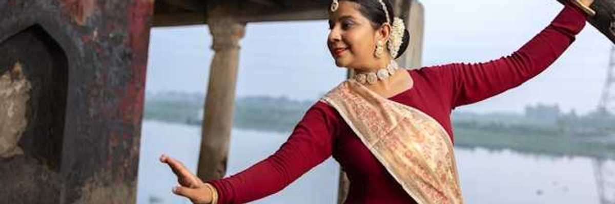An Indian woman wearing jewerly and a sash dancing next to a river