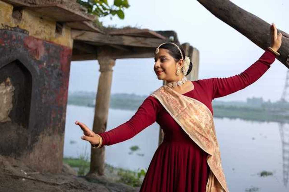 An Indian woman wearing jewerly and a sash dancing next to a river
