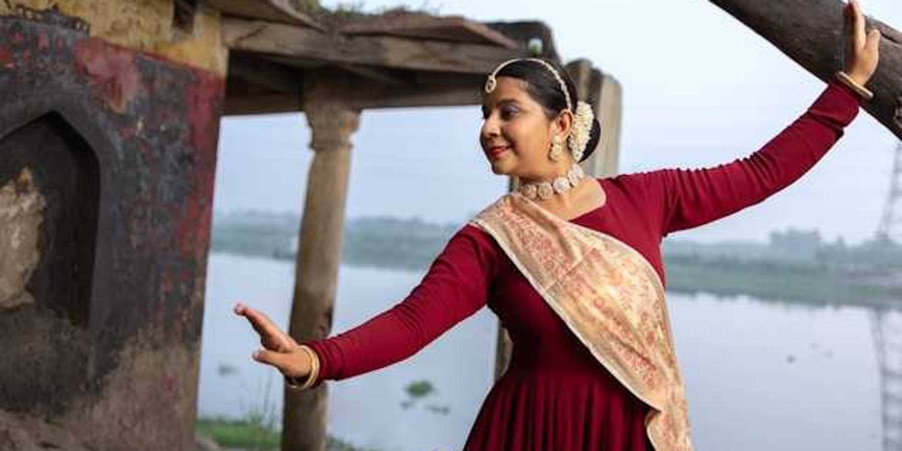An Indian woman wearing jewerly and a sash dancing next to a river