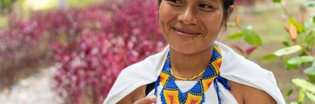 An indigenous woman with a colorful necklace smiling at someone to her right