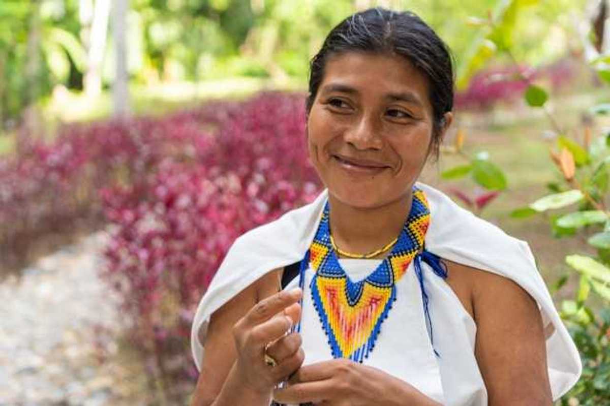 An indigenous woman with a colorful necklace smiling at someone to her right