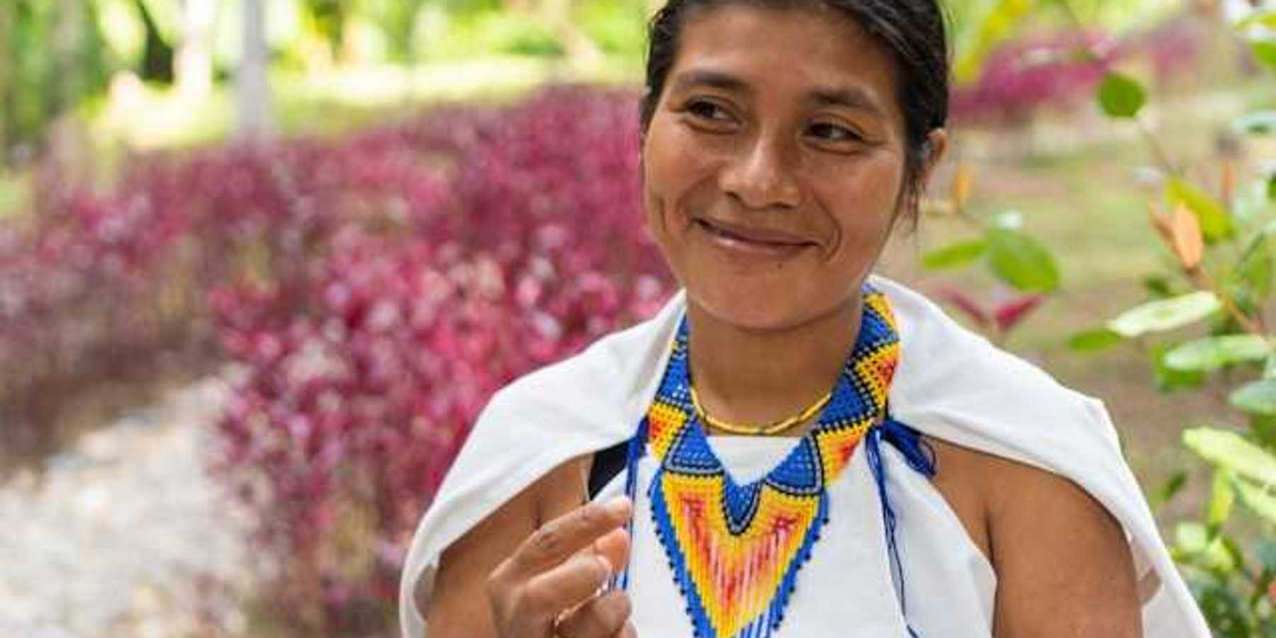 An indigenous woman with a colorful necklace smiling at someone to her right