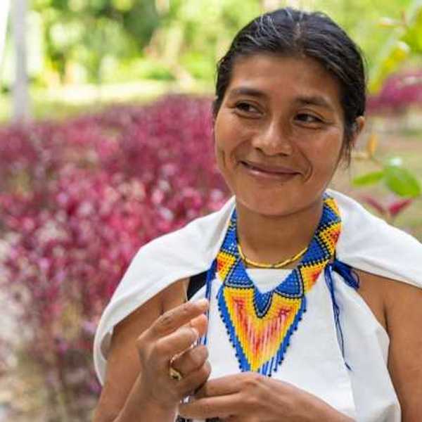 An indigenous woman with a colorful necklace smiling at someone to her right