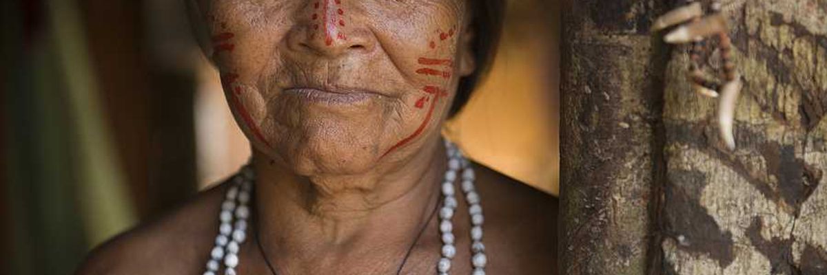 An indigenous woman with red paint on her face standing next to a tree