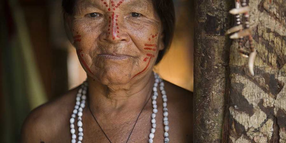 An indigenous woman with red paint on her face standing next to a tree